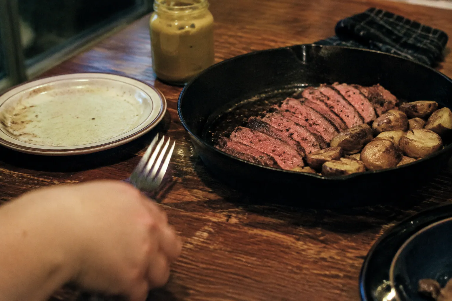 夜の家庭の食卓で、黒胡椒を効かせたステーキとローストポテトが鋳物鍋に残る
