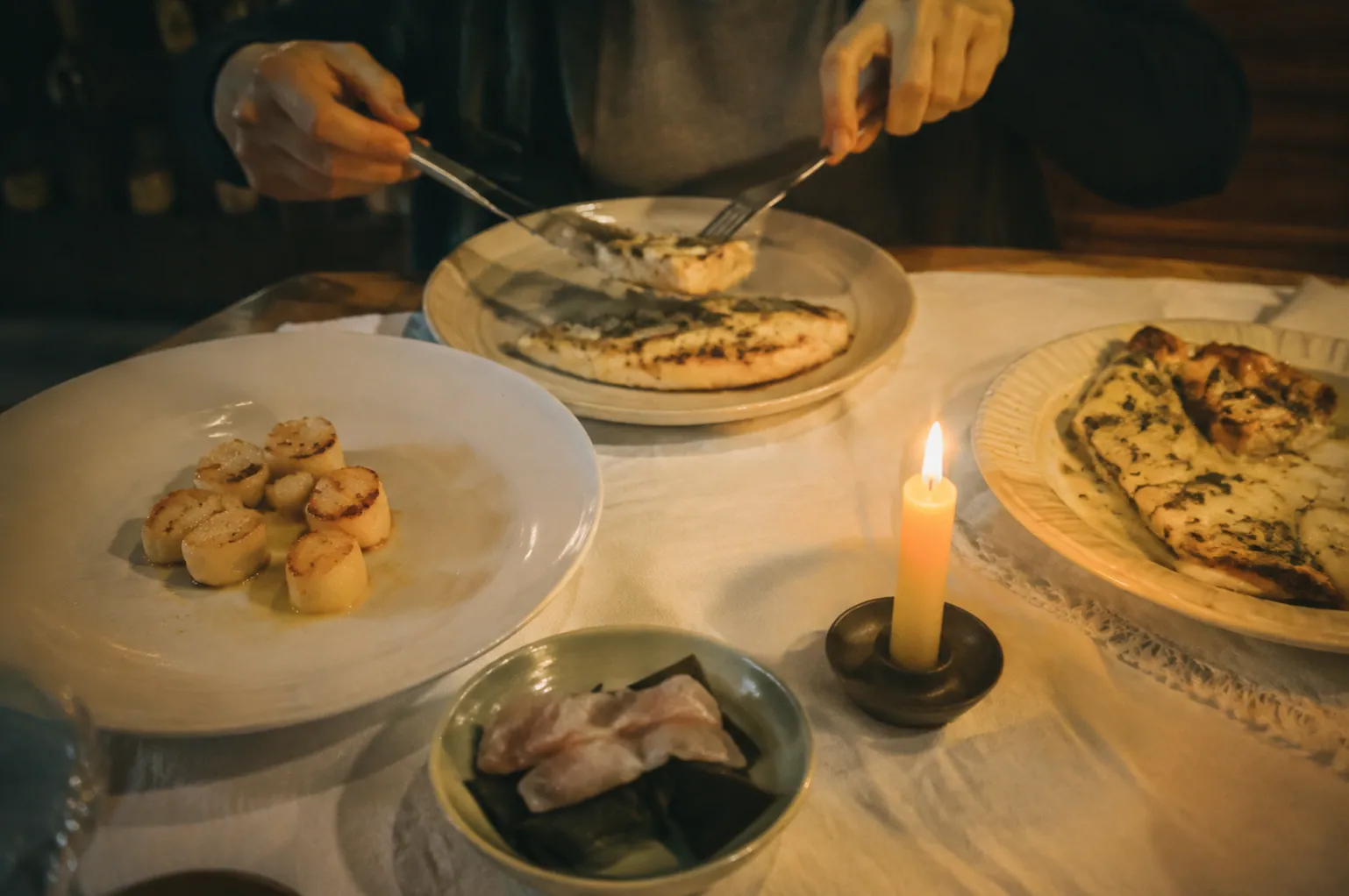 蝋燭を灯した家庭の食卓で、白身魚と帆立を取り分ける手