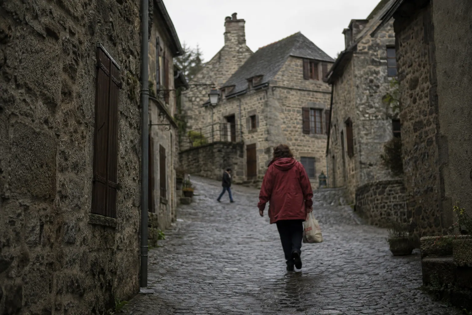 冬の終わりの石造りの村で、赤い上着の住人が濡れた坂道を歩く