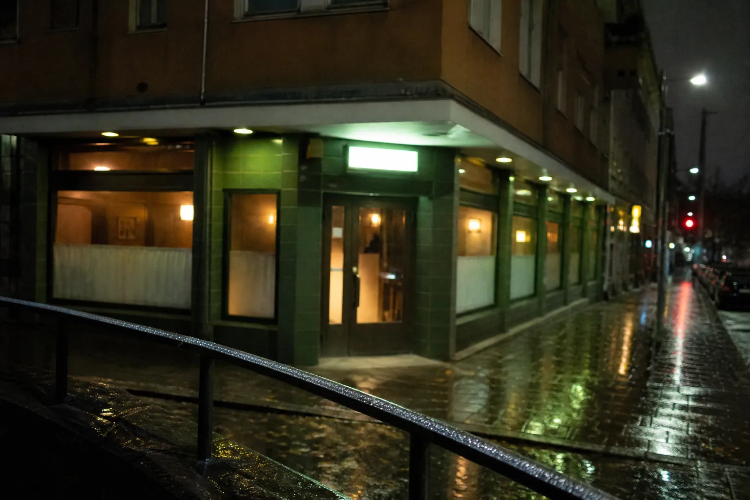 雨に濡れた夜の街角に灯る緑色の小さな店