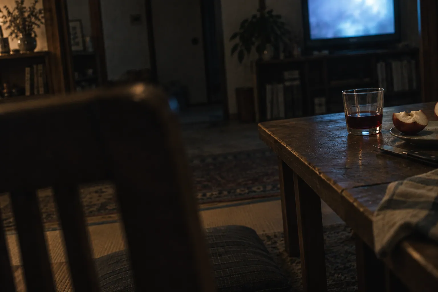 青いテレビの残光が漂う夜の居間で、食べかけのリンゴと赤ワインが食卓の端に残る