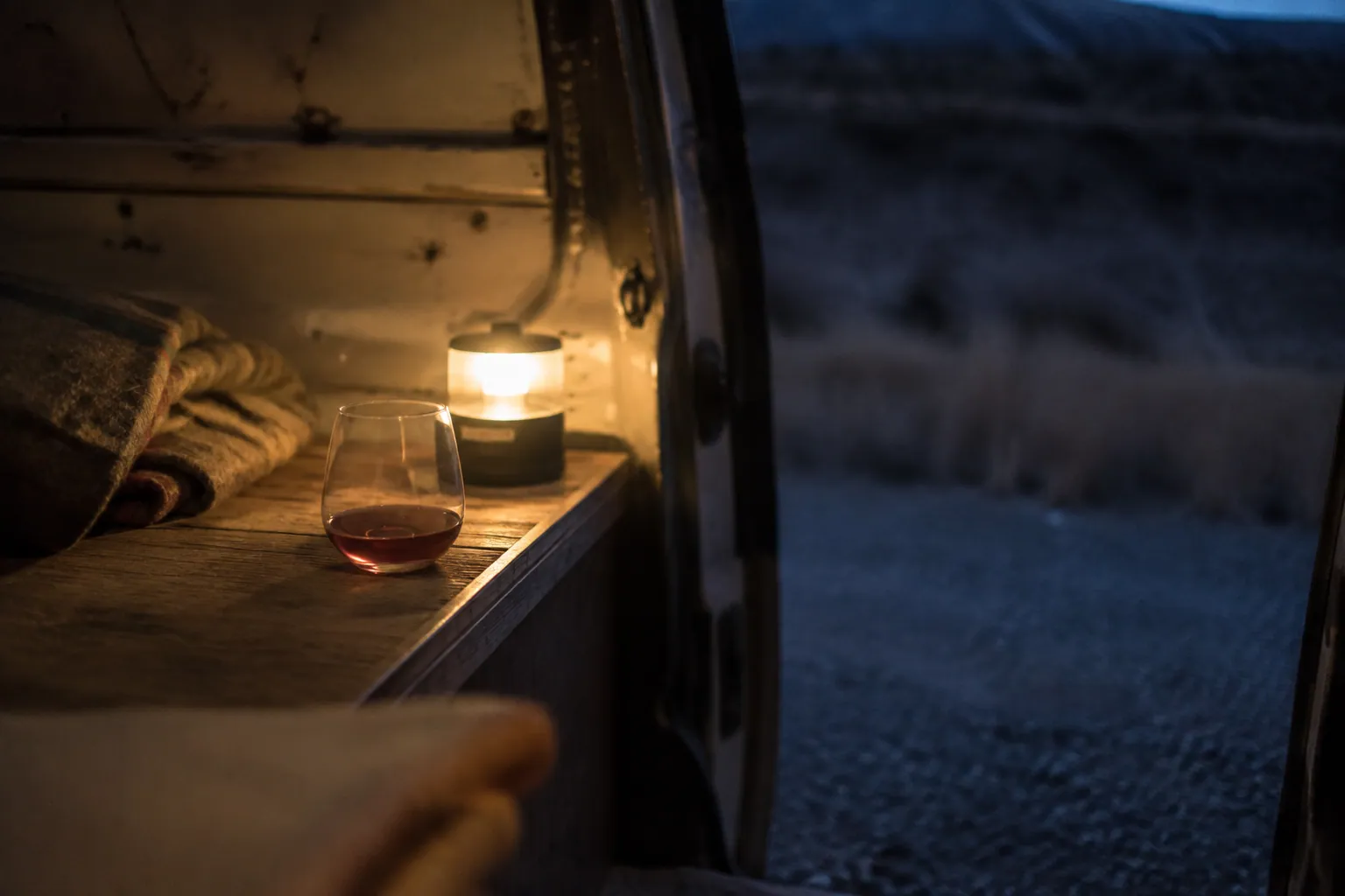 夜を過ごすため停めた古いヴァンの車内、毛布と小さなランタン、赤ワインの一杯