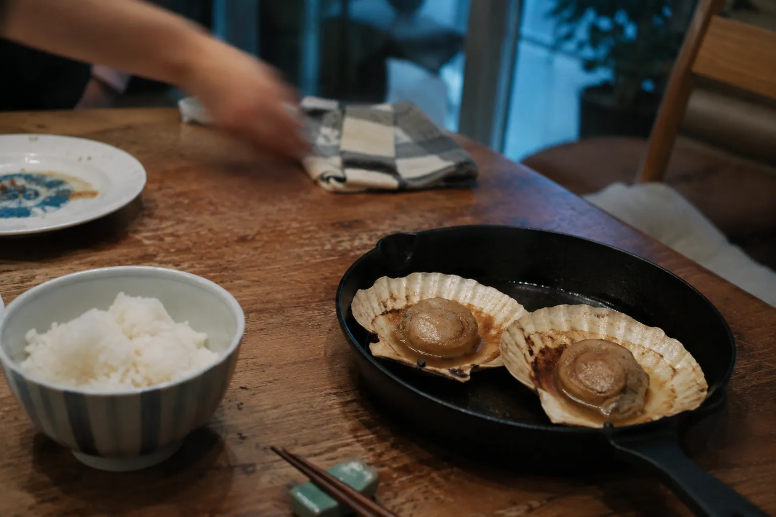 家庭の食卓で、鋳物の鍋にホタテのバター醤油焼きとご飯が並ぶ