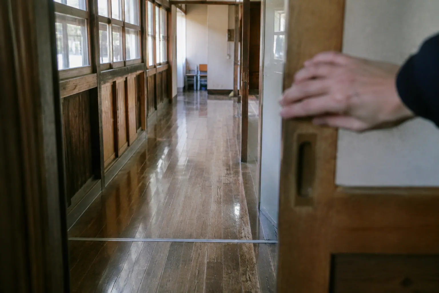 西日の差す古い木造校舎の廊下で、手が引き戸を静かに閉めている