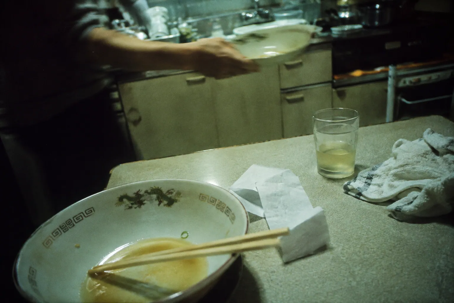 深夜の日本の台所で、食べ終えた丼と白ワインを残して流しへ向かう手