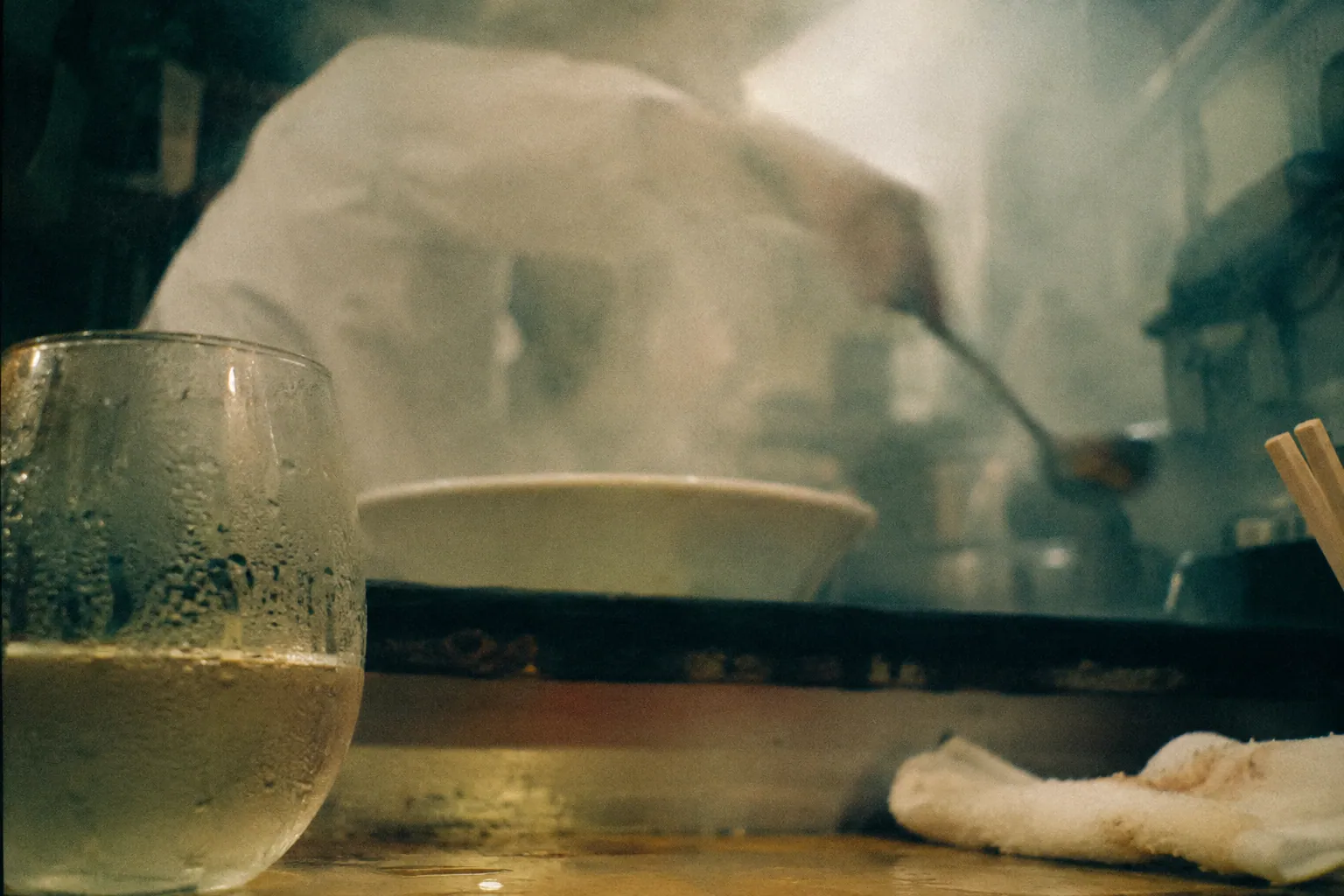 結露した白ワインのグラスと、湯気に隠れて輪郭だけが残るラーメンの丼