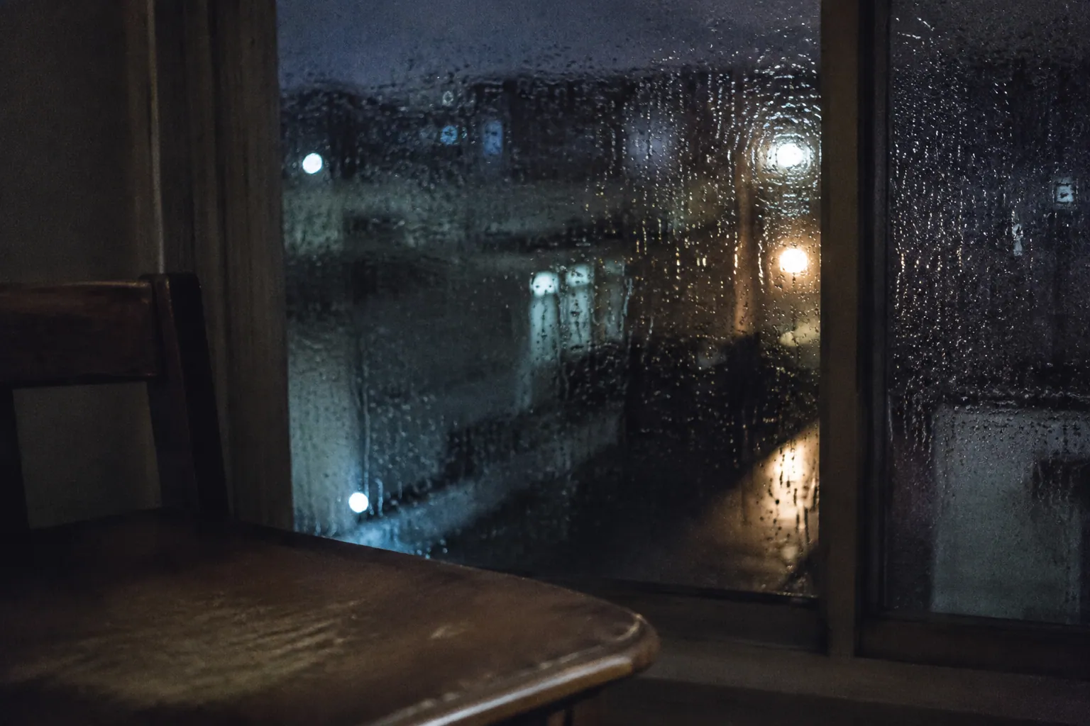 雨粒のついた夜の窓と、暗い室内の空席